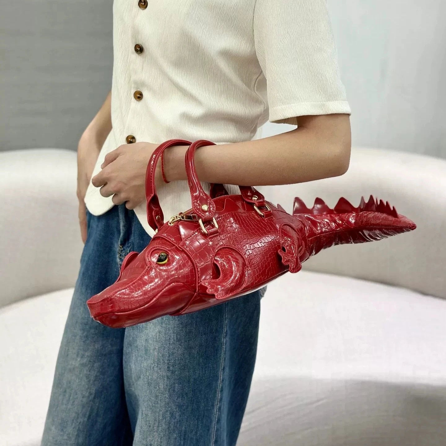 Person holding a red alligator-shaped handbag against a neutral background