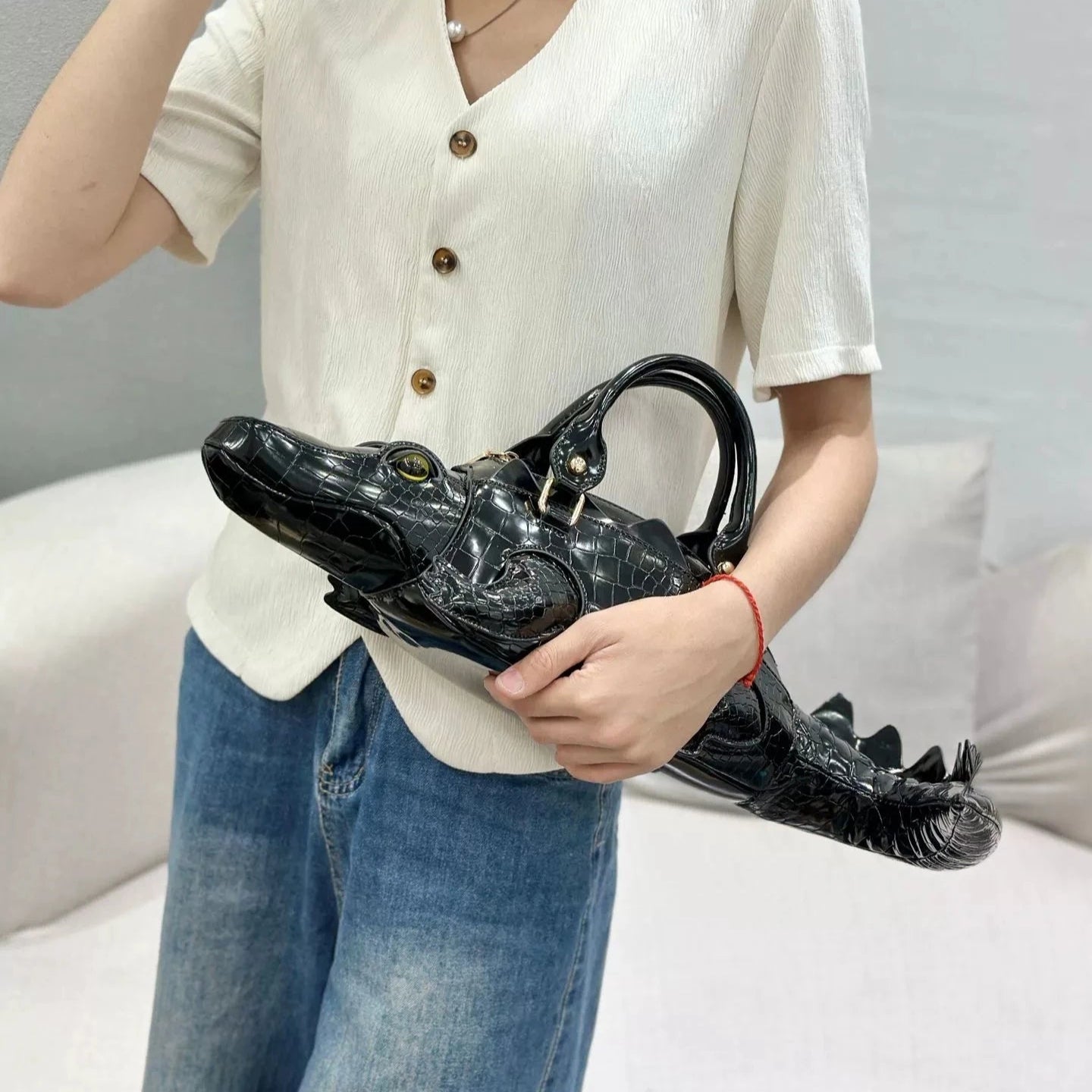 Person holding a black crocodile-shaped handbag against a neutral background