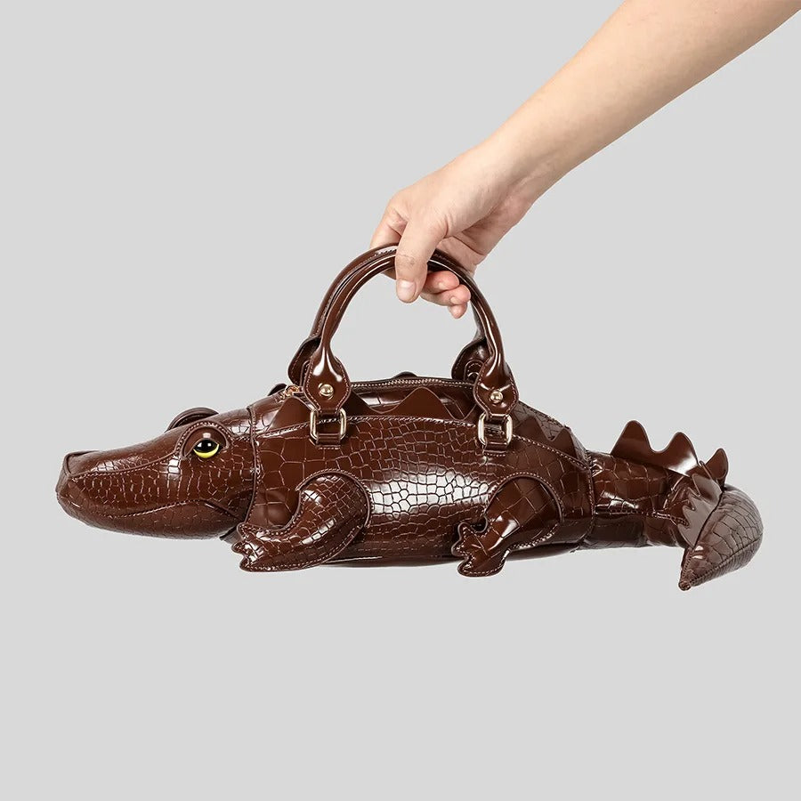 Brown alligator-shaped handbag held by a hand on a light gray background