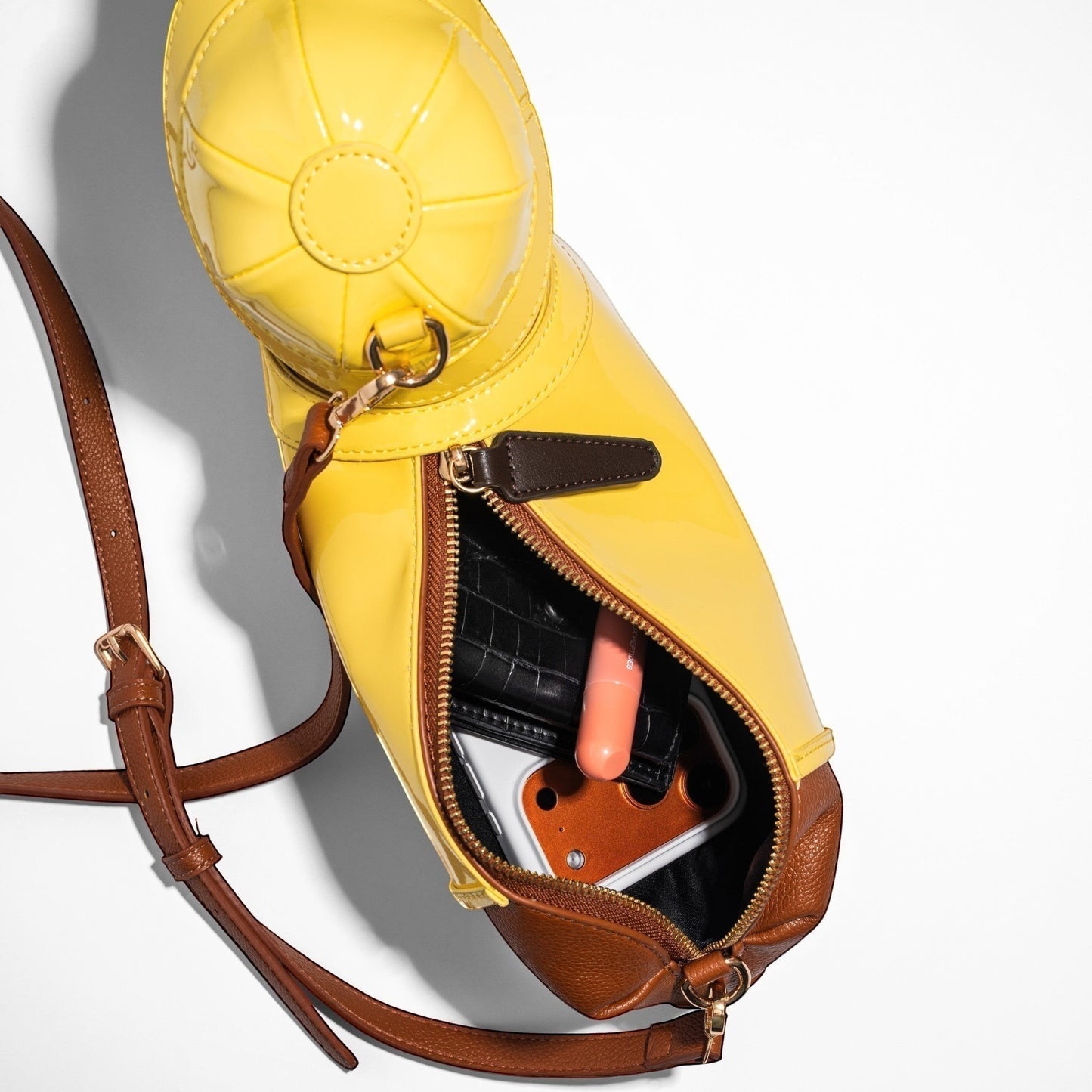 Pordein yellow patent leather dachshund shoulder bag with brown trim and strap. Contains wallet, phone, and lipstick.