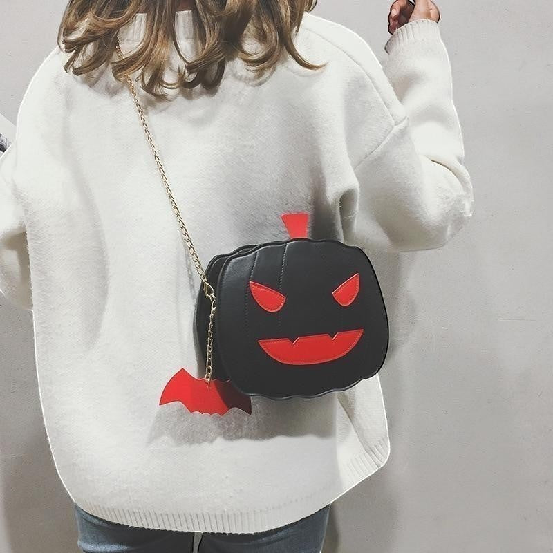 Pordein black PU leather Halloween pumpkin bag with red face details and bat charm, worn crossbody.