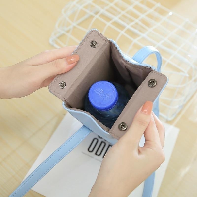 Pordein light blue PU leather mini milk carton bag with adjustable strap, holding a water bottle.