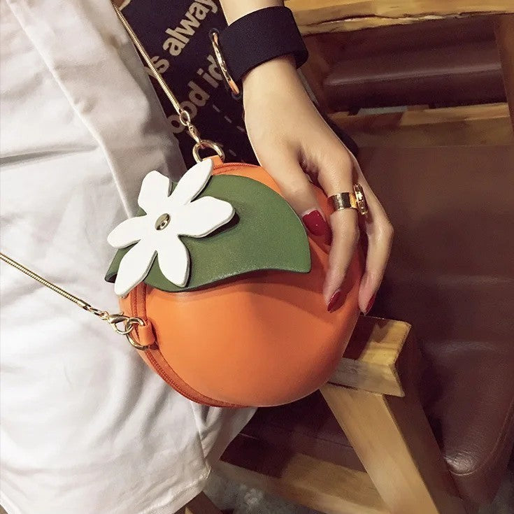 Pordein orange PU leather mini bag shaped like a fruit with a white flower and green leaf detail. Can be worn as a handbag or clutch.