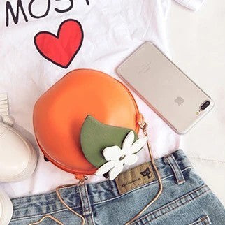 Pordein orange PU leather mini bag shaped like a fruit with a green leaf and white flower detail. Can be worn as a crossbody or clutch.