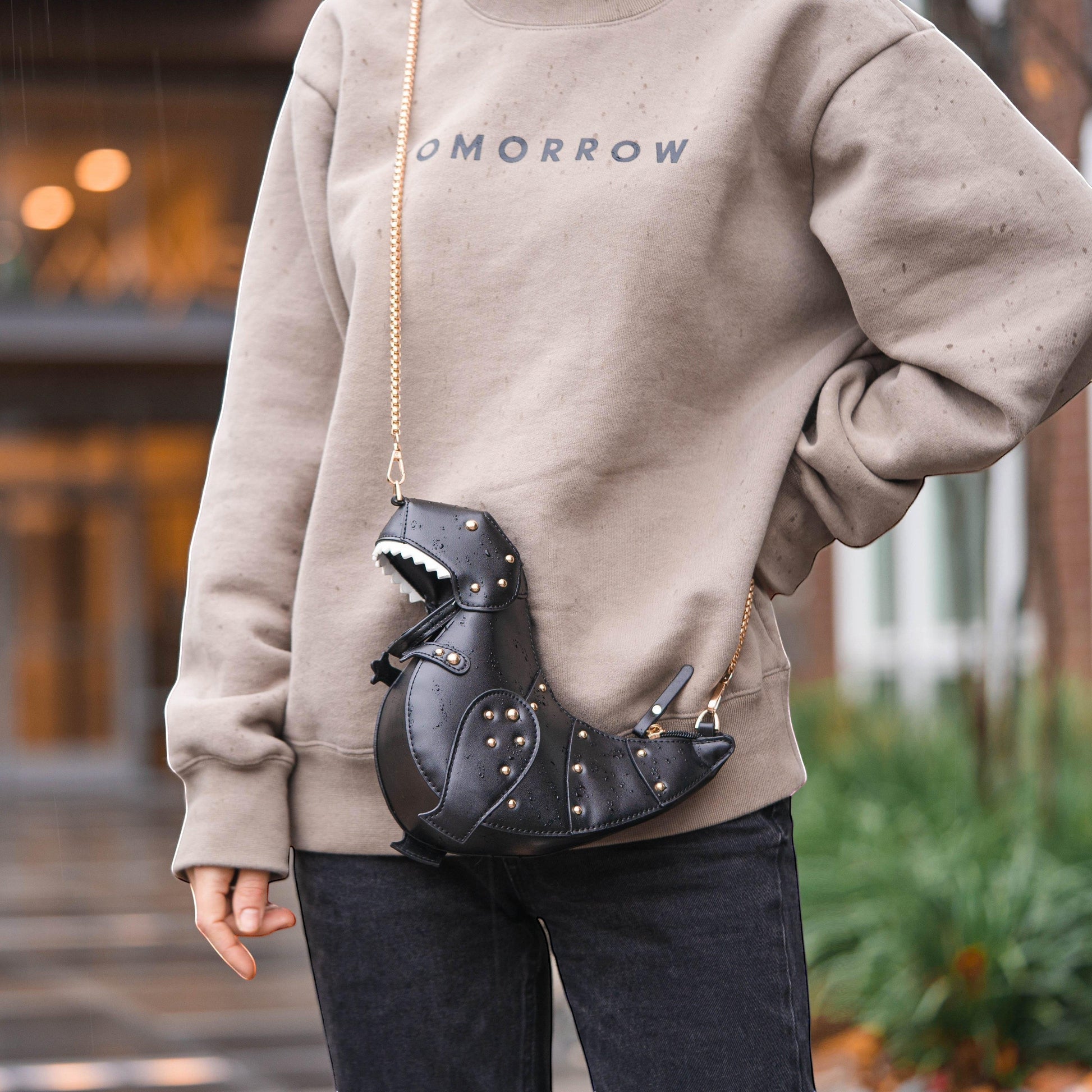 Pordein black vegan leather Rex Mini Bag shaped like a dinosaur with gold studs and a chain strap.