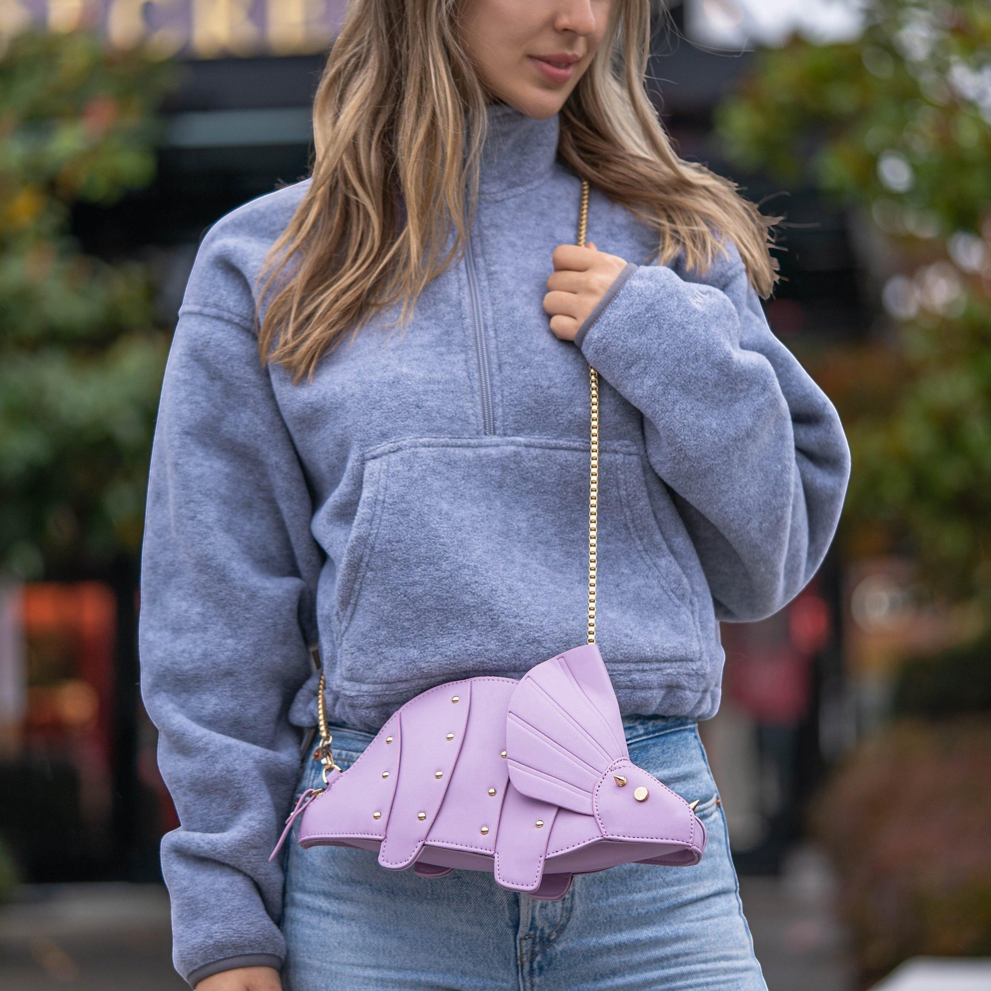 Pordein lavender vegan leather Triceratops mini bag with studded detail and gold chain strap, worn crossbody by a woman.