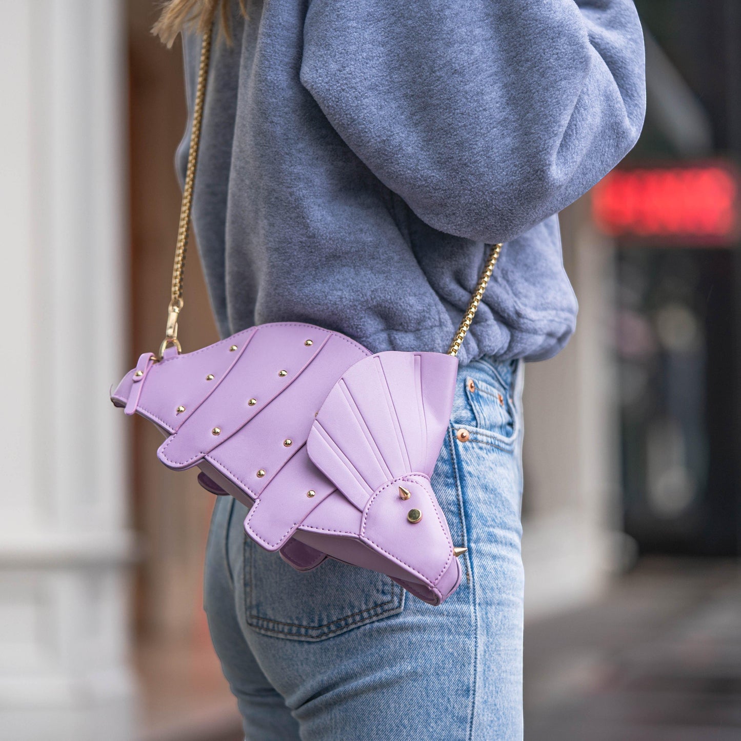 Pordein lavender vegan leather Triceratops mini bag with gold stud details and a gold chain strap, worn crossbody.
